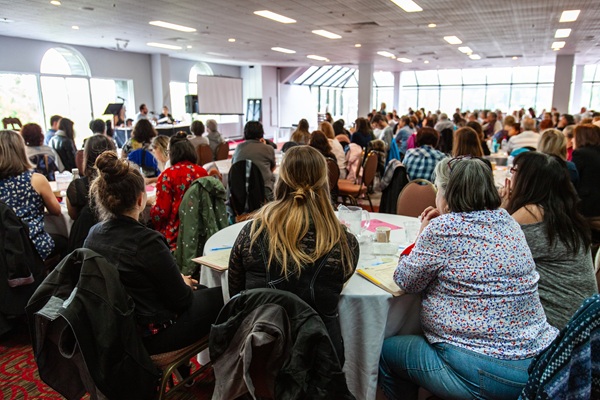 Large group of people seated at round tables in a conference room attending a corporate event or seminar.