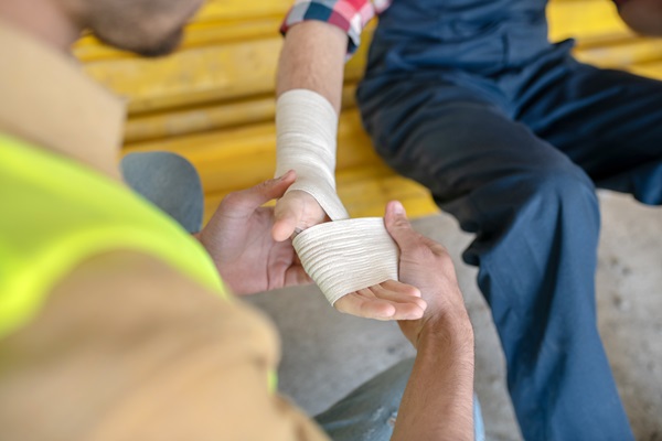 Close-up of building worker applying bandage on his injured coworker's hand.